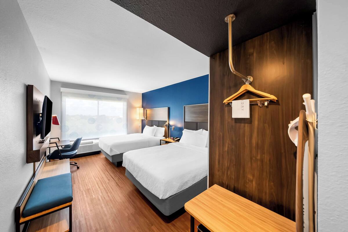 A hotel room with two beds, a desk, a chair, a TV, a coat rack, and a window with a view.