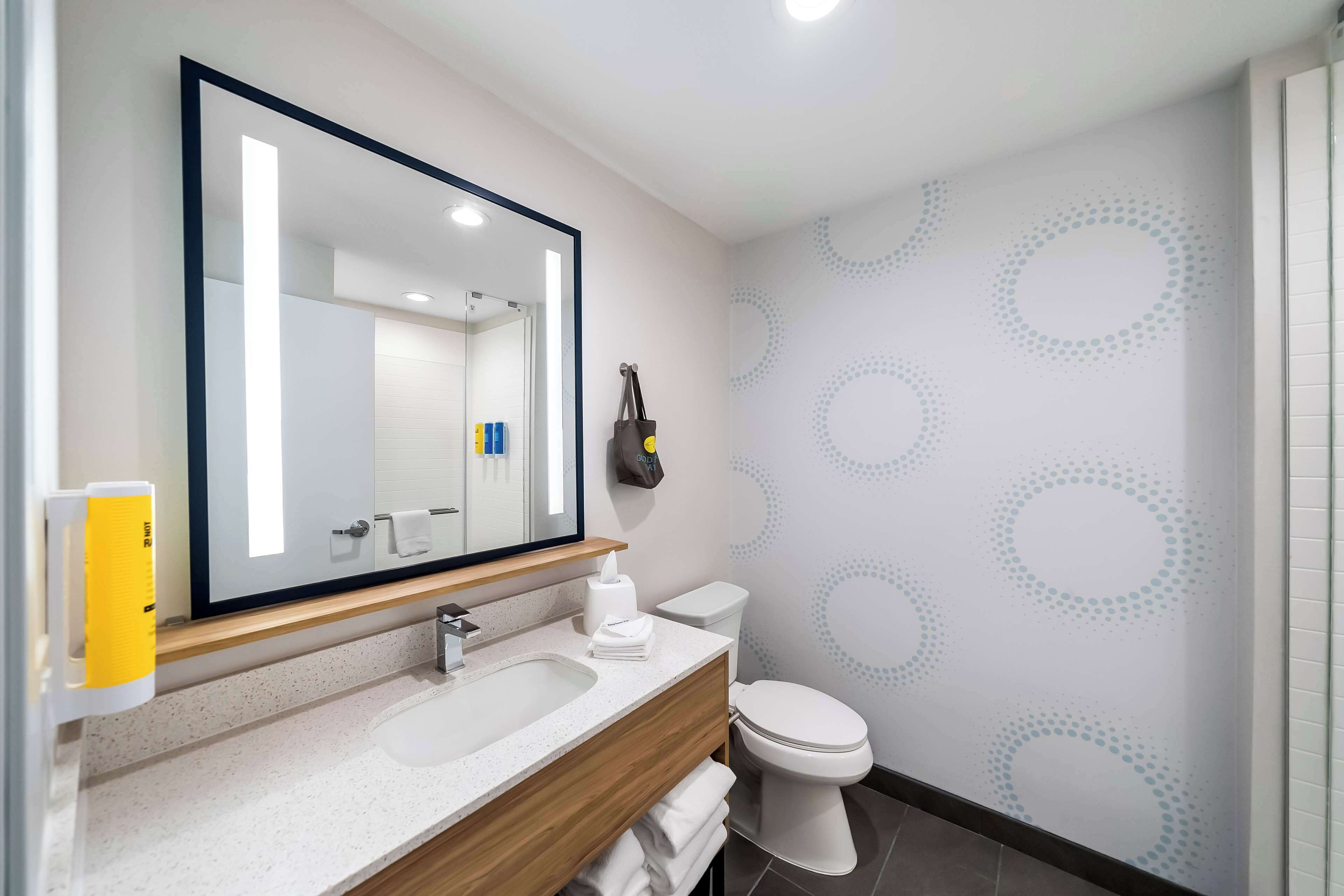 A modern bathroom with a large mirror, a sink, and a toilet.