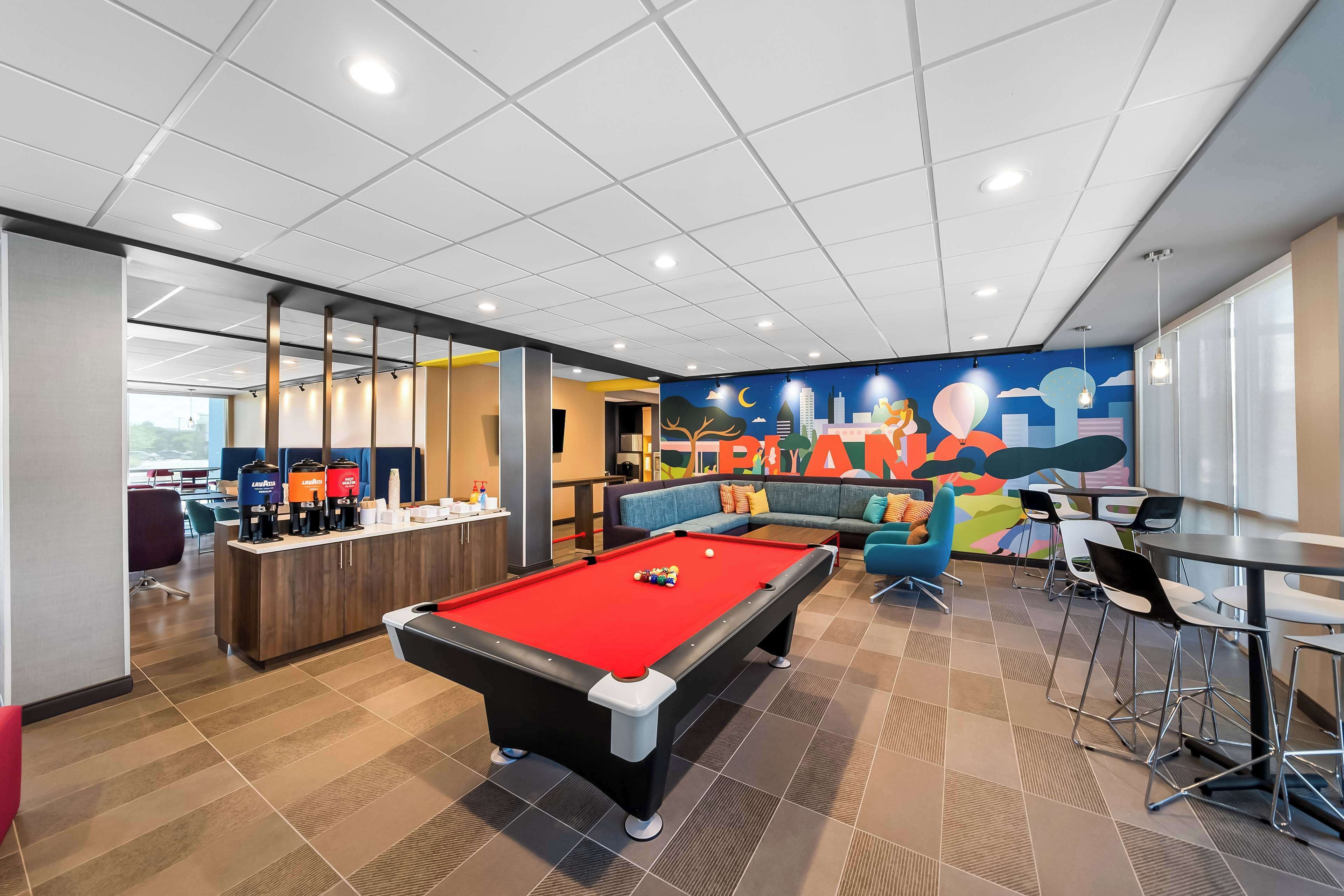 A pool table with a red felt surface, a bar area with a counter and stools, and a colorful mural on the wall.
