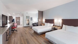 Hotellihuone, jossa on kaksi sänkyä, työpöytä, jossa on tietokone, tuoli, pieni pöytä ja peili.