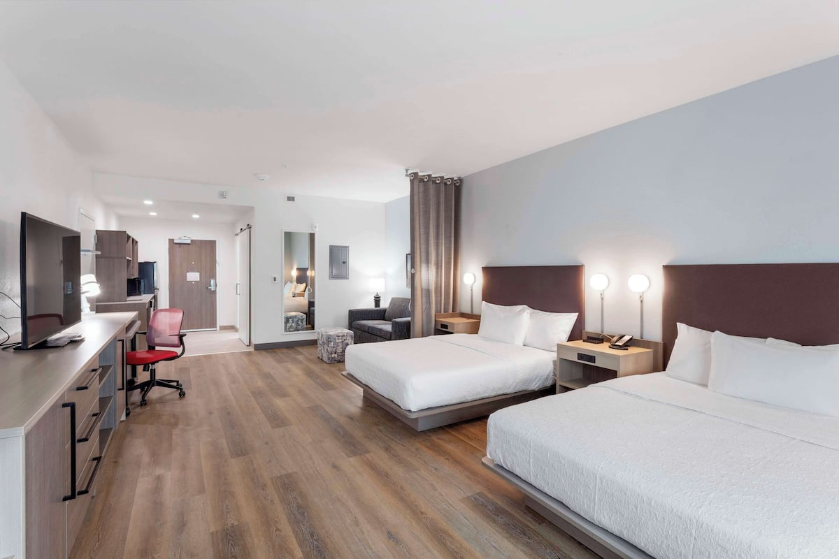 A hotel room with two beds, a desk with a computer, a chair, a small table, and a mirror.