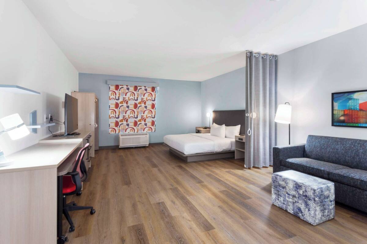 A hotel room with a bed, a desk with a computer, a sofa, and a small table.