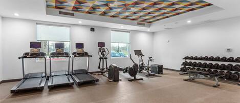 A gym with treadmills, elliptical machines, and a wall of dumbbells.
