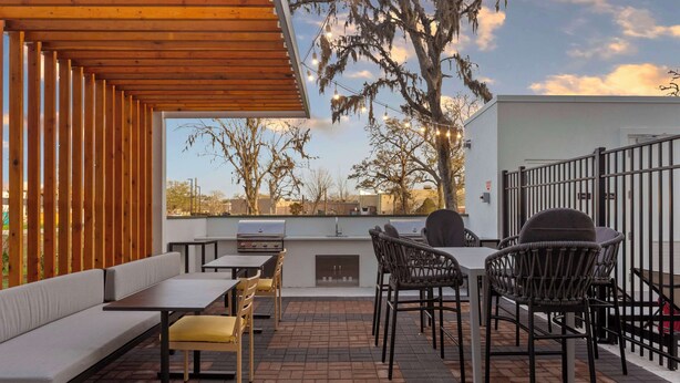 Ulkoterassi, jossa on grilli, istuimia ja näkymä puille ja rakennuksille.