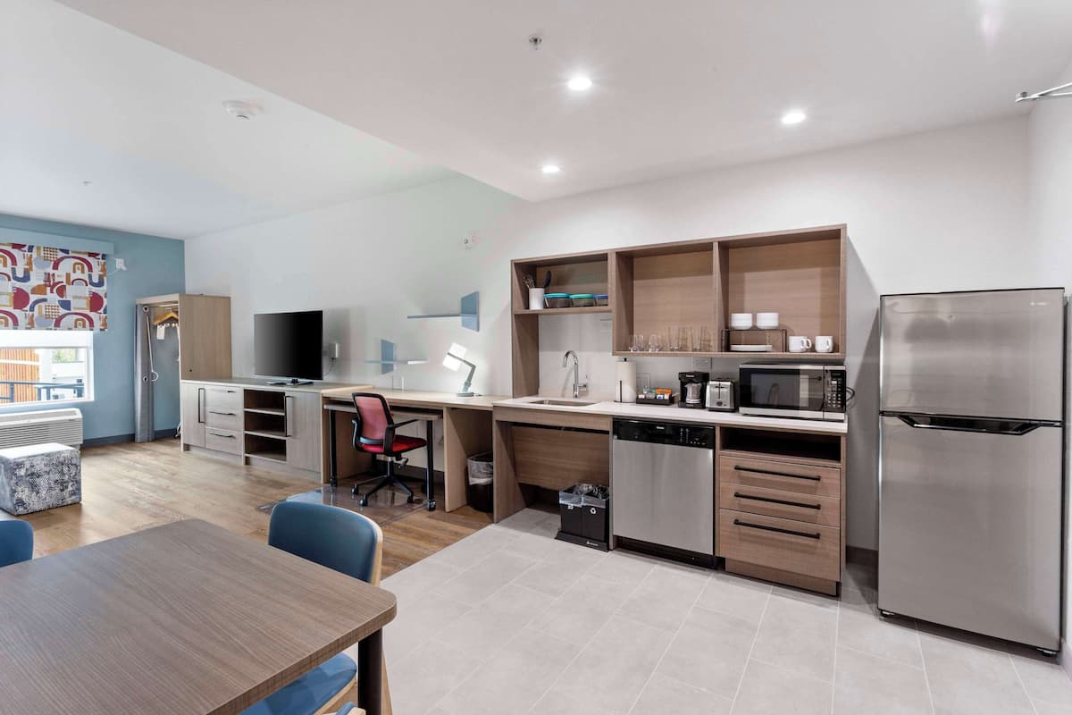 A modern kitchen with a dishwasher, microwave, and refrigerator. There is a dining table with chairs and a TV in the corner.