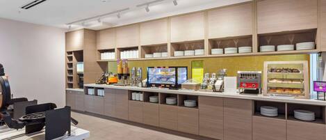 Een moderne ontbijtbar met een koffieautomaat, een vitrine met gebak, en keurig geordonde borden en kommen.