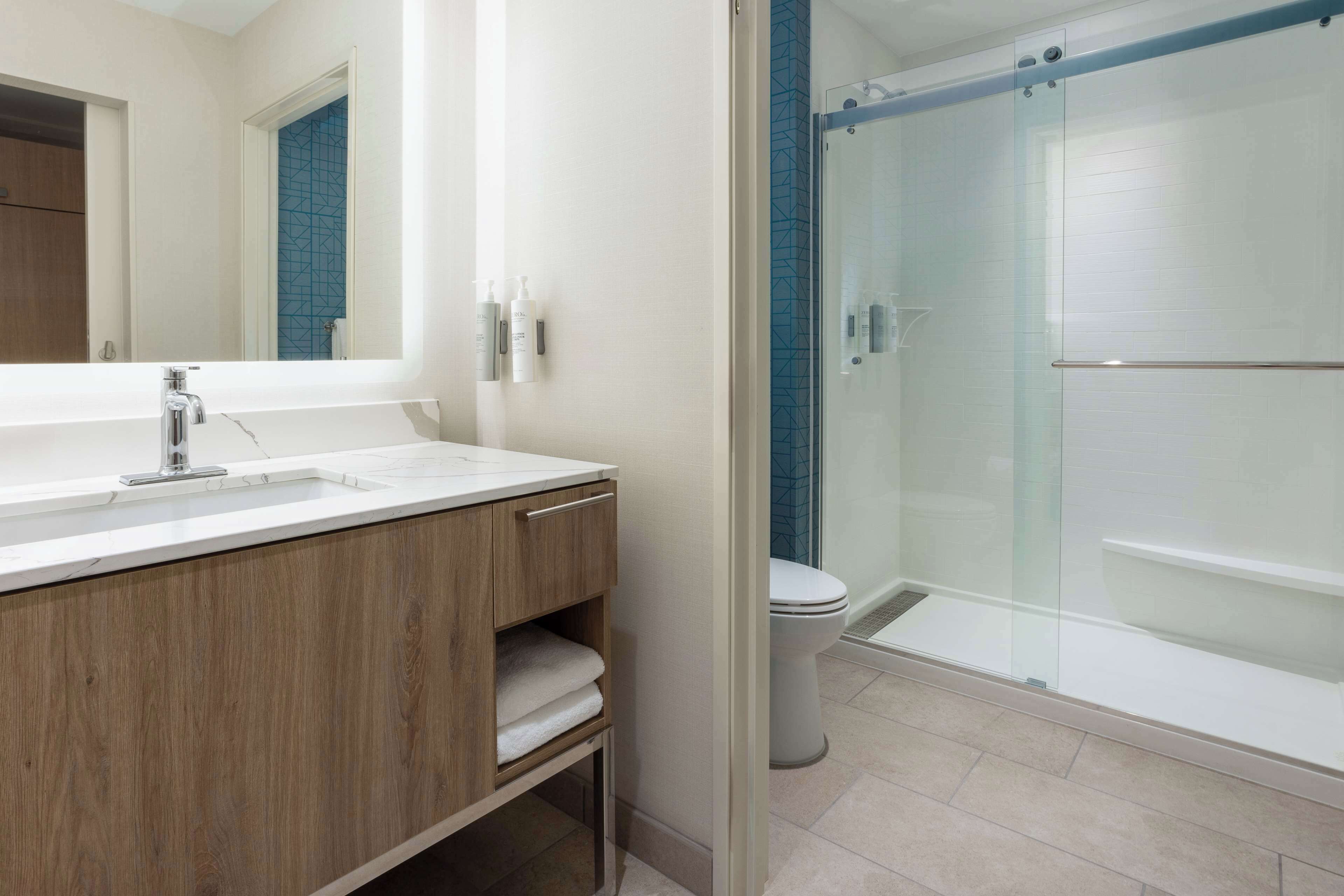 A modern bathroom with a wooden vanity, a large mirror, and a glass-enclosed shower area.