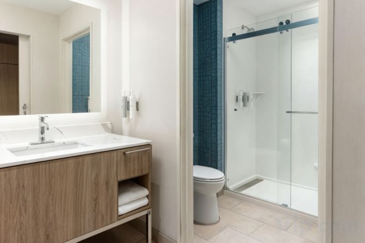 Een moderne badkamer met een glazen douchecabine, een witte wastafel en een spiegel.