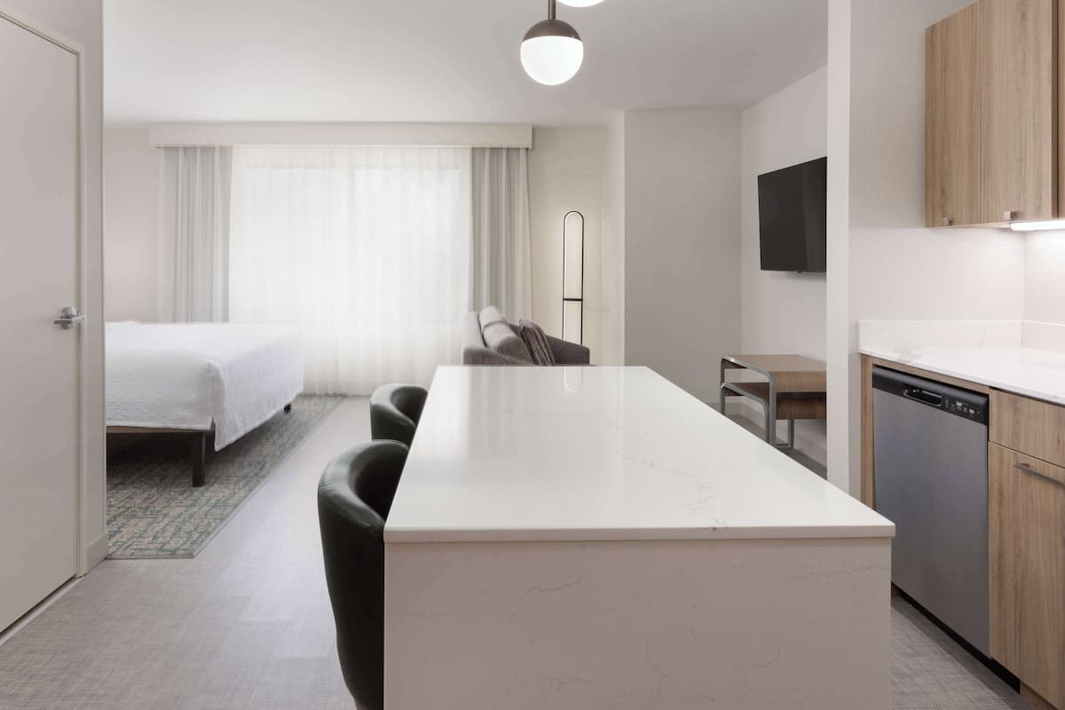 Ein modernes Hotelzimmer mit einem großen Bett, einer Essecke und einer Küche mit Geschirrspüler.