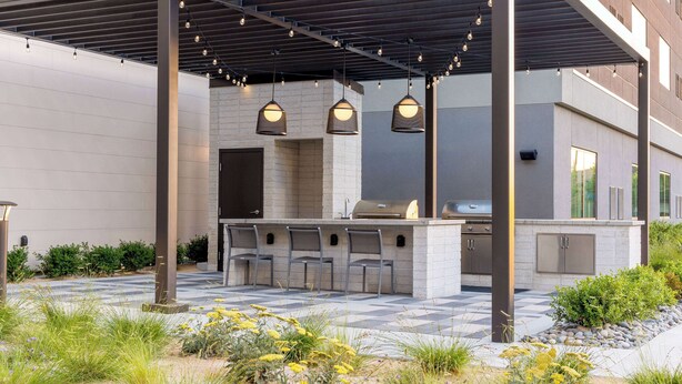 Eine Terrasse im Freien mit Grill, Barhocker und hängenden Lichtern.