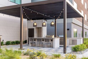 Une terrasse extérieure équipée d’un barbecue, de sièges de bar et de guirlandes lumineuses.