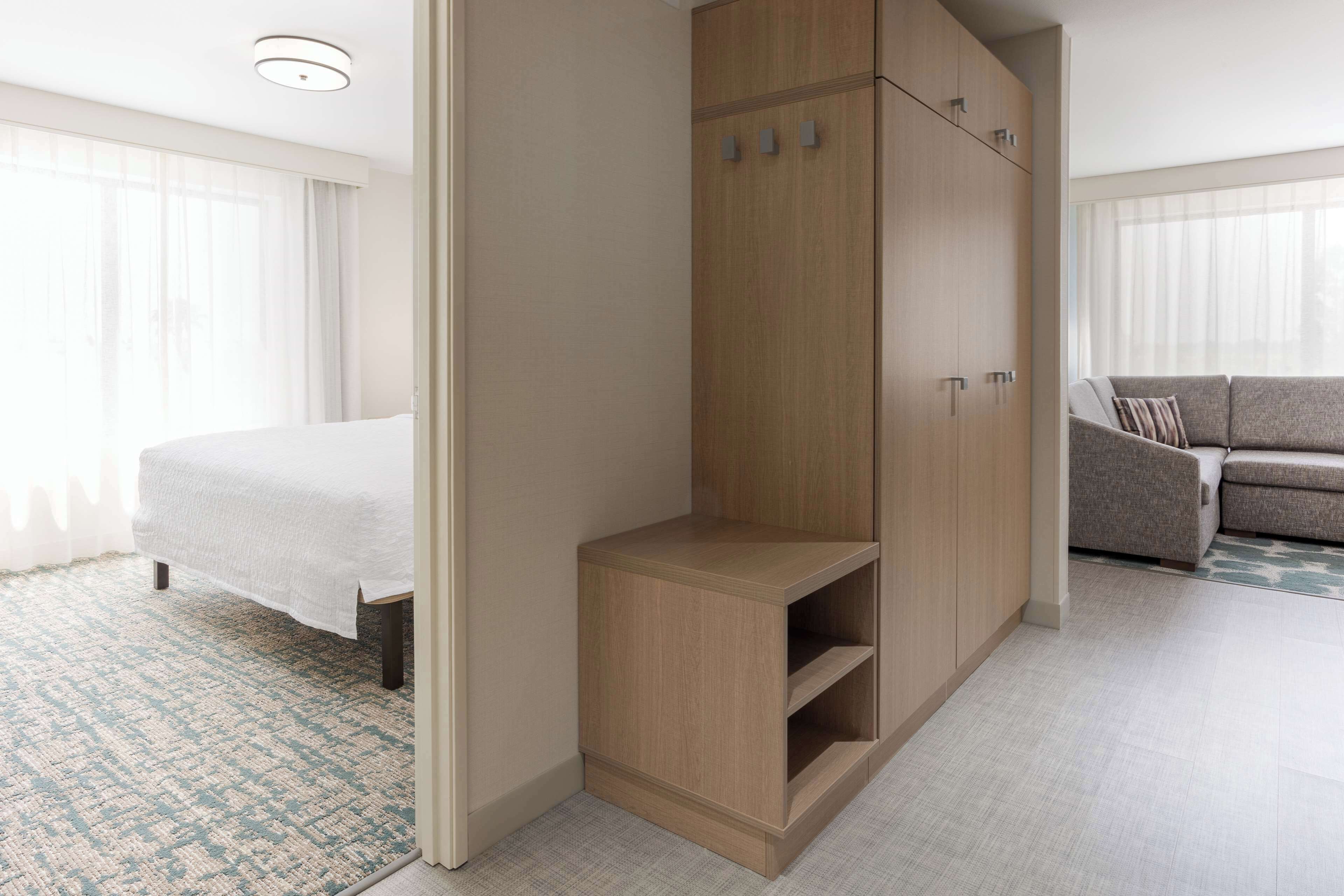 A hotel room with a bed, a wooden wardrobe, a seating area with a sofa, and a patterned carpet.