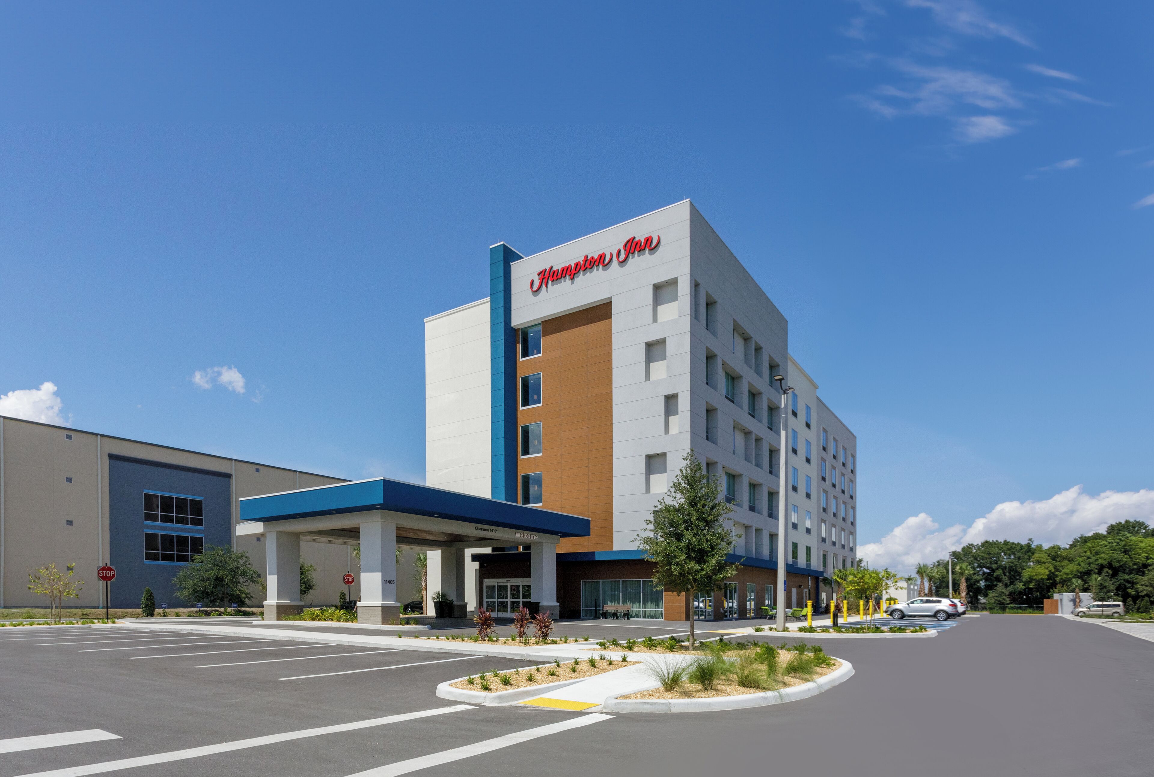 A Hampton Inn hotel with a modern design, featuring a blue and white color scheme, a central entrance, and a parking lot.