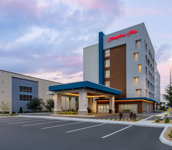 Un hotel Hampton Inn con diseño moderno, que cuenta con un amplio acceso con área techada y un estacionamiento al frente.