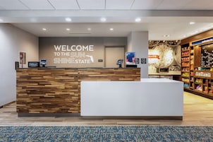 Ein Empfangsschalter mit einem Schild, auf dem 'Welcome to the Sun Shine State' steht, sowie Schildern mit 'Hilton' und 'Fats'.