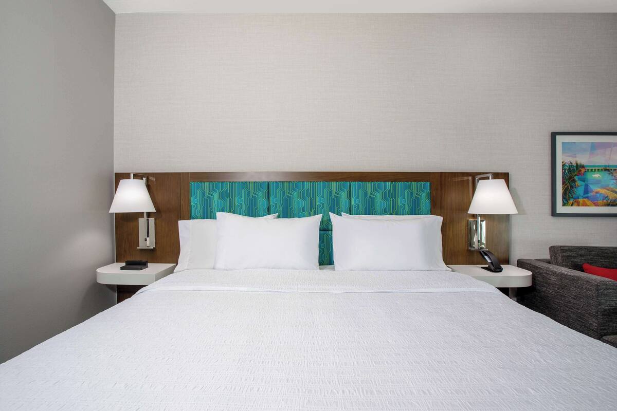 A hotel room with a large bed, two bedside tables with lamps, a wooden headboard, and a painting on the wall.