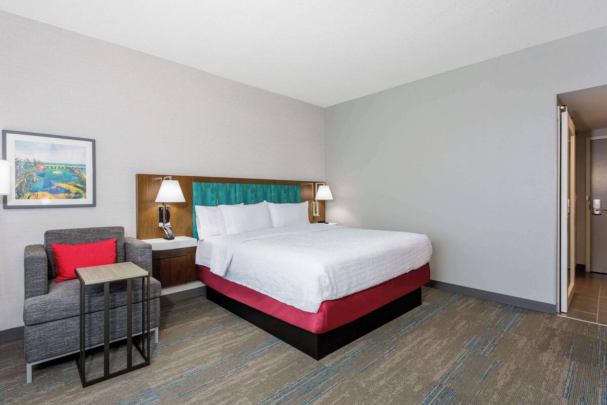 A hotel room with a bed, a nightstand, a chair, and a small table.
