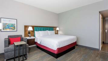 Ein Hotelzimmer mit Bett, Nachttisch, Sessel und kleinem Tisch.