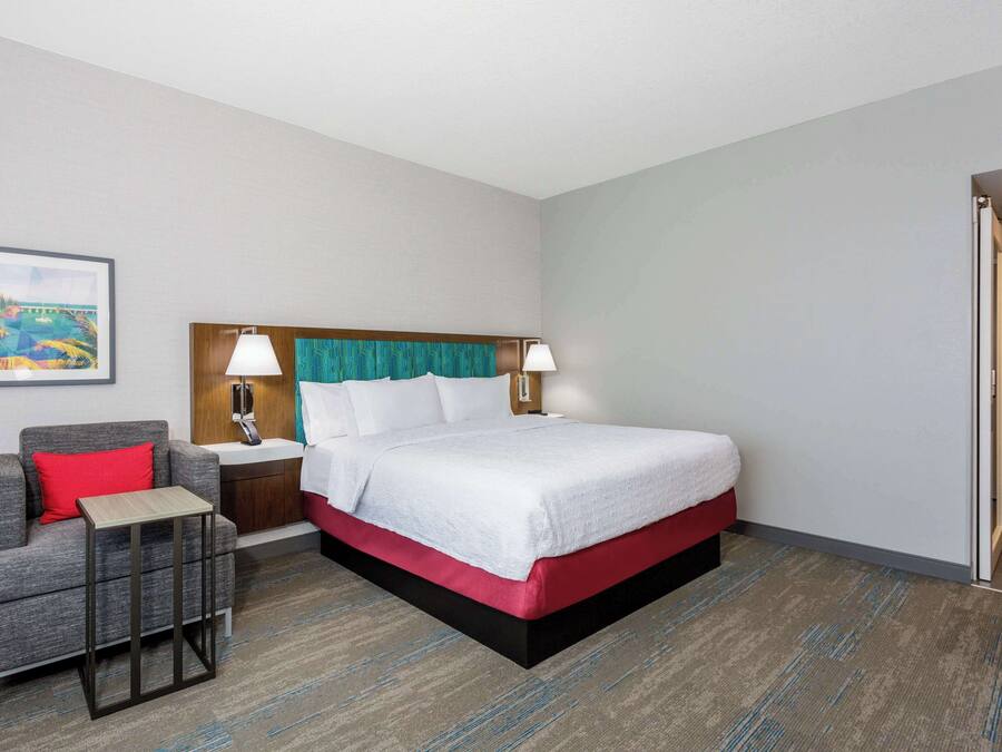 Ein Hotelzimmer mit Bett, Nachttisch, Sessel und kleinem Tisch.