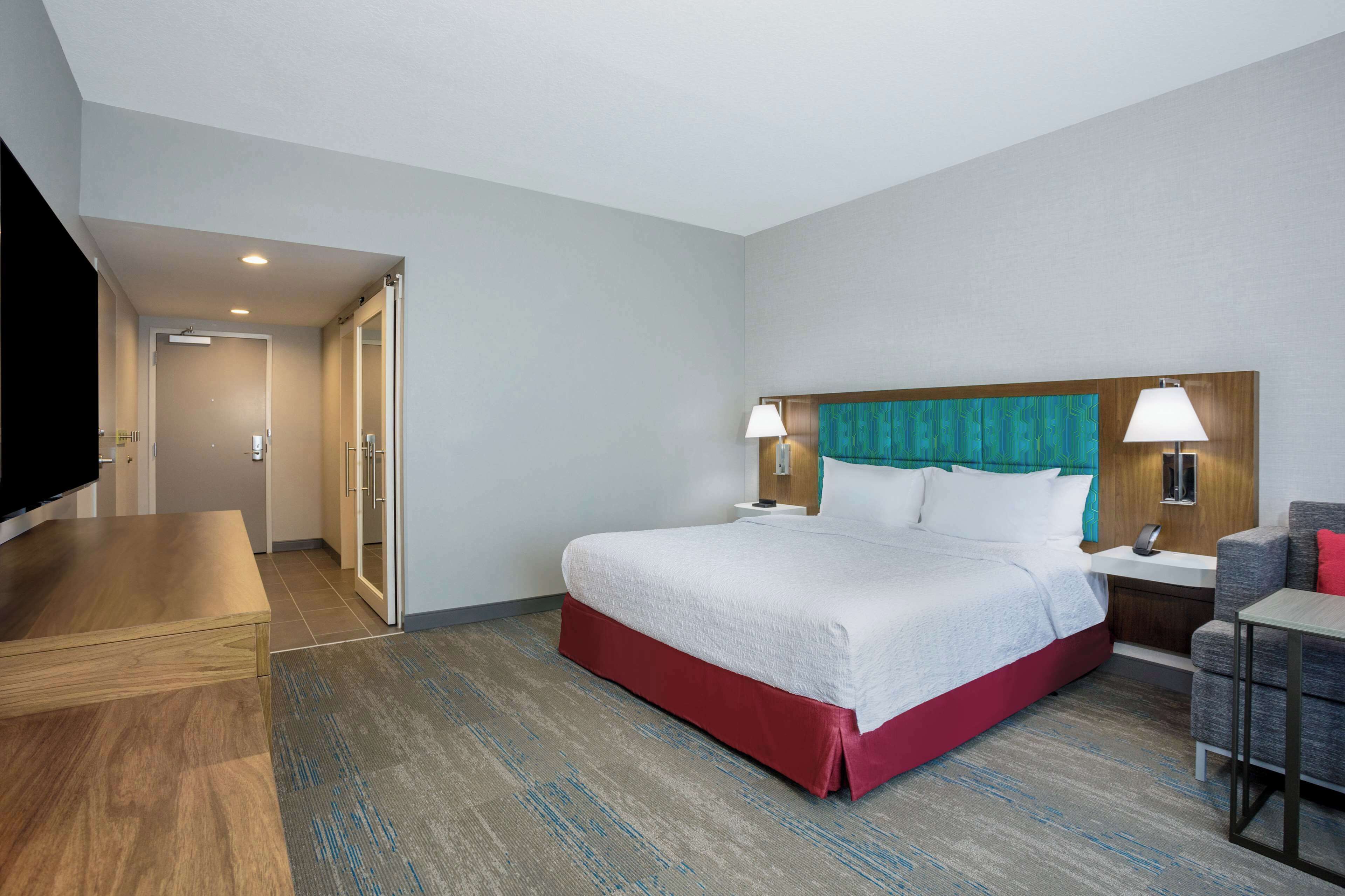A hotel room with a bed, bedside tables, a desk, and a TV.