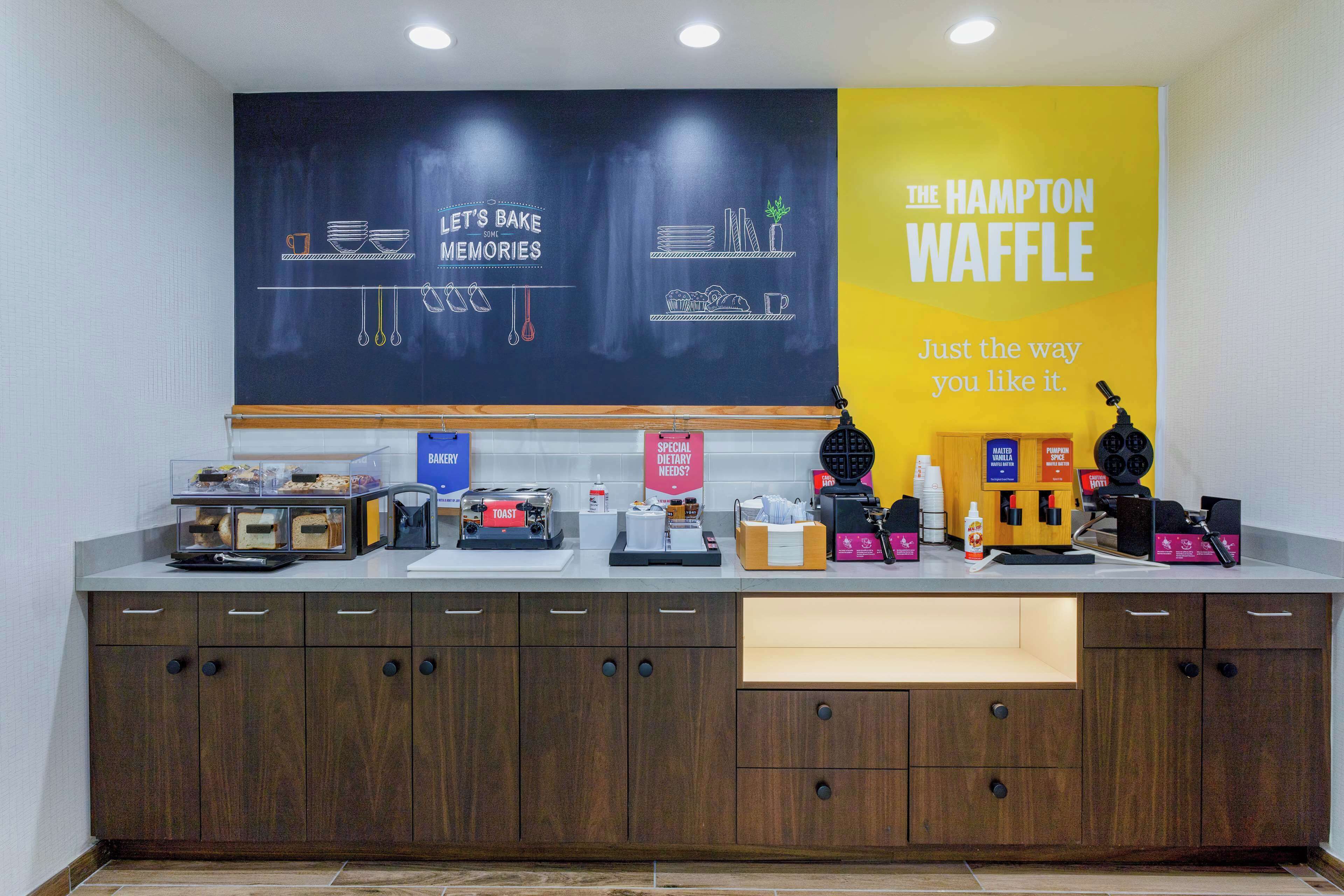 A kitchen counter with a chalkboard displaying "Let's Bake Memories" and "The Hampton Waffle" sign.