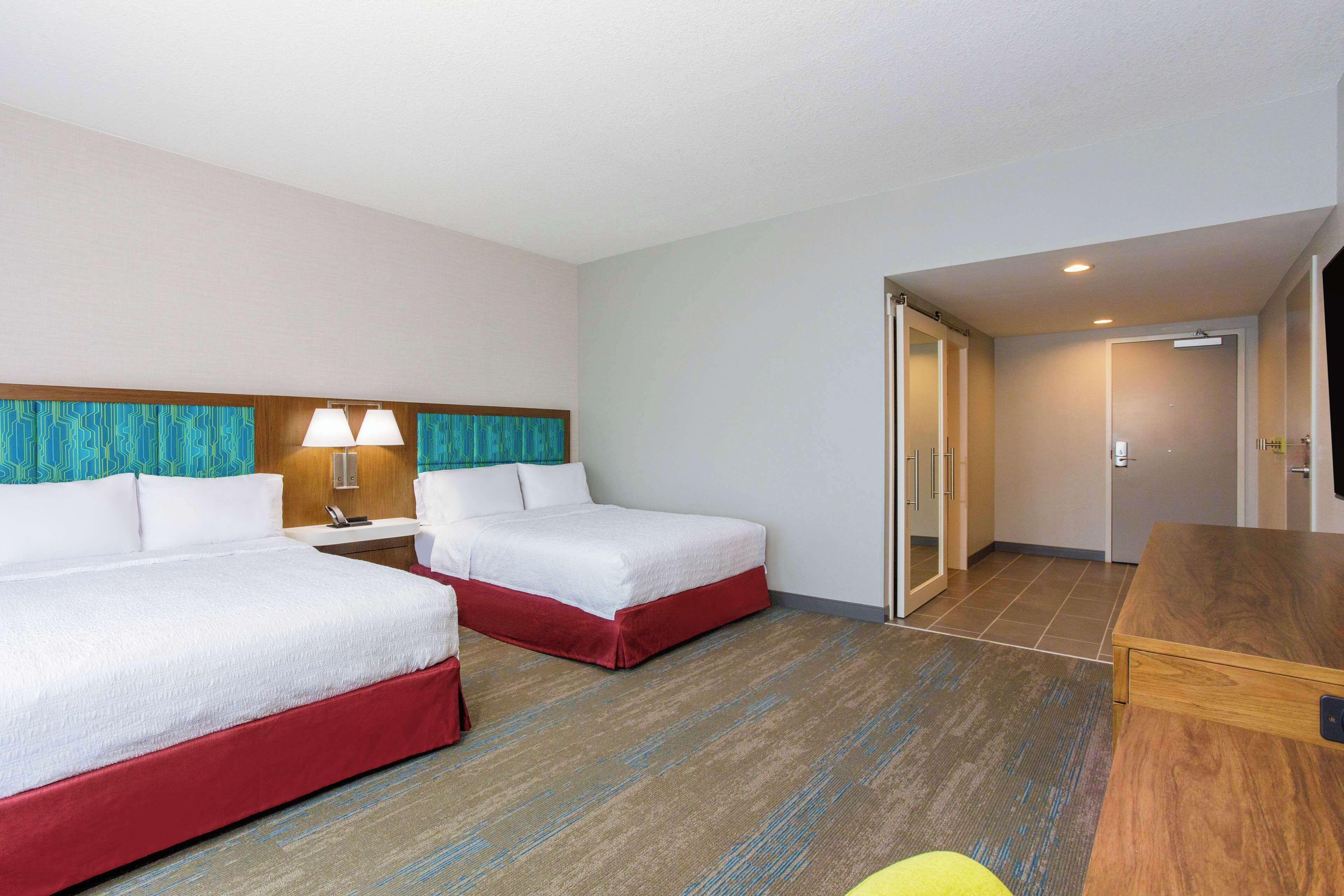 A hotel room with two beds, a desk, and a bathroom visible through an open door.