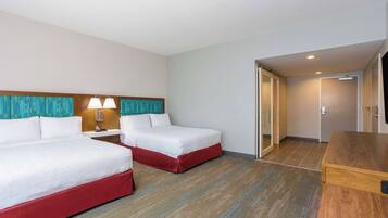 A hotel room with two beds, a desk, and a bathroom visible through an open door.