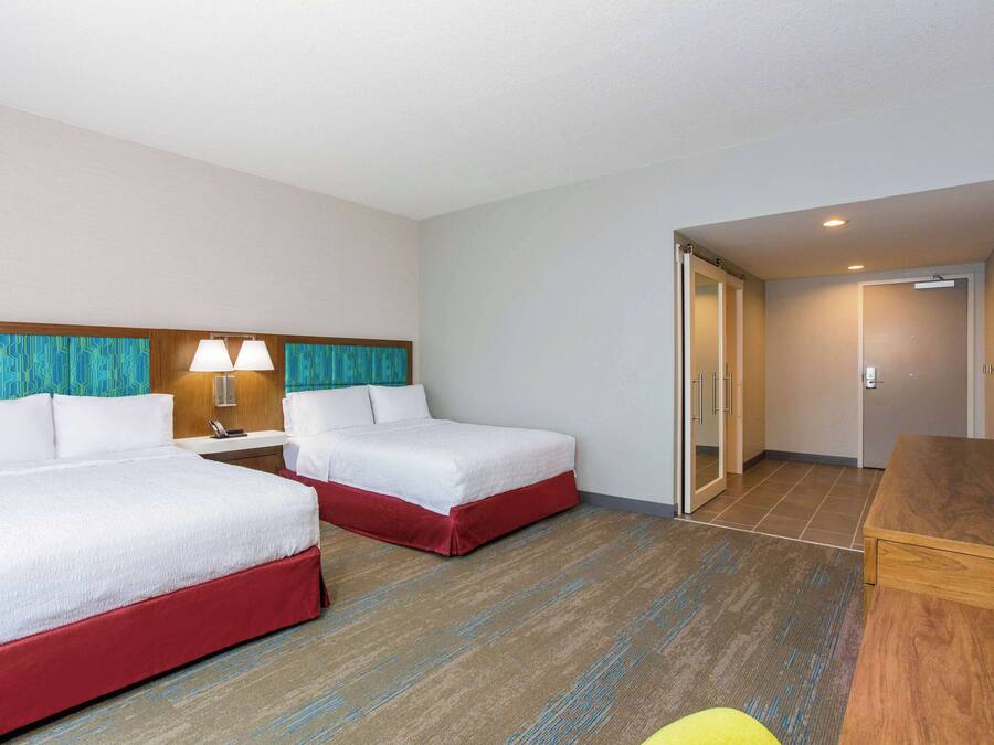 A hotel room with two beds, a desk, and a bathroom visible through an open door.