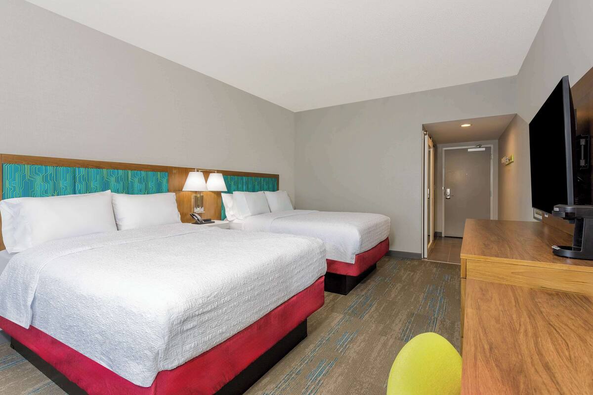 A hotel room with two beds, a desk, and a television.
