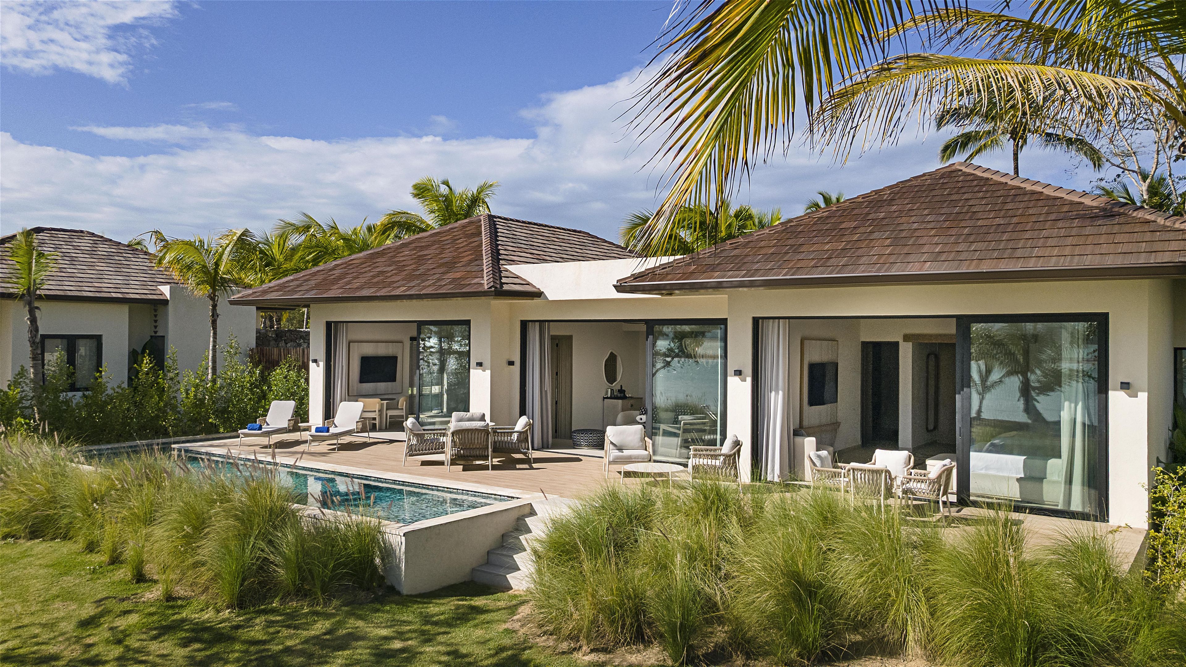Una villa moderna con piscina, mobiliario exterior y un gran ventanal que da a un patio.