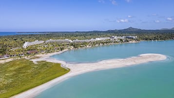 Vista aérea de un resort con playa, un gran complejo hotelero y una montaña al fondo.