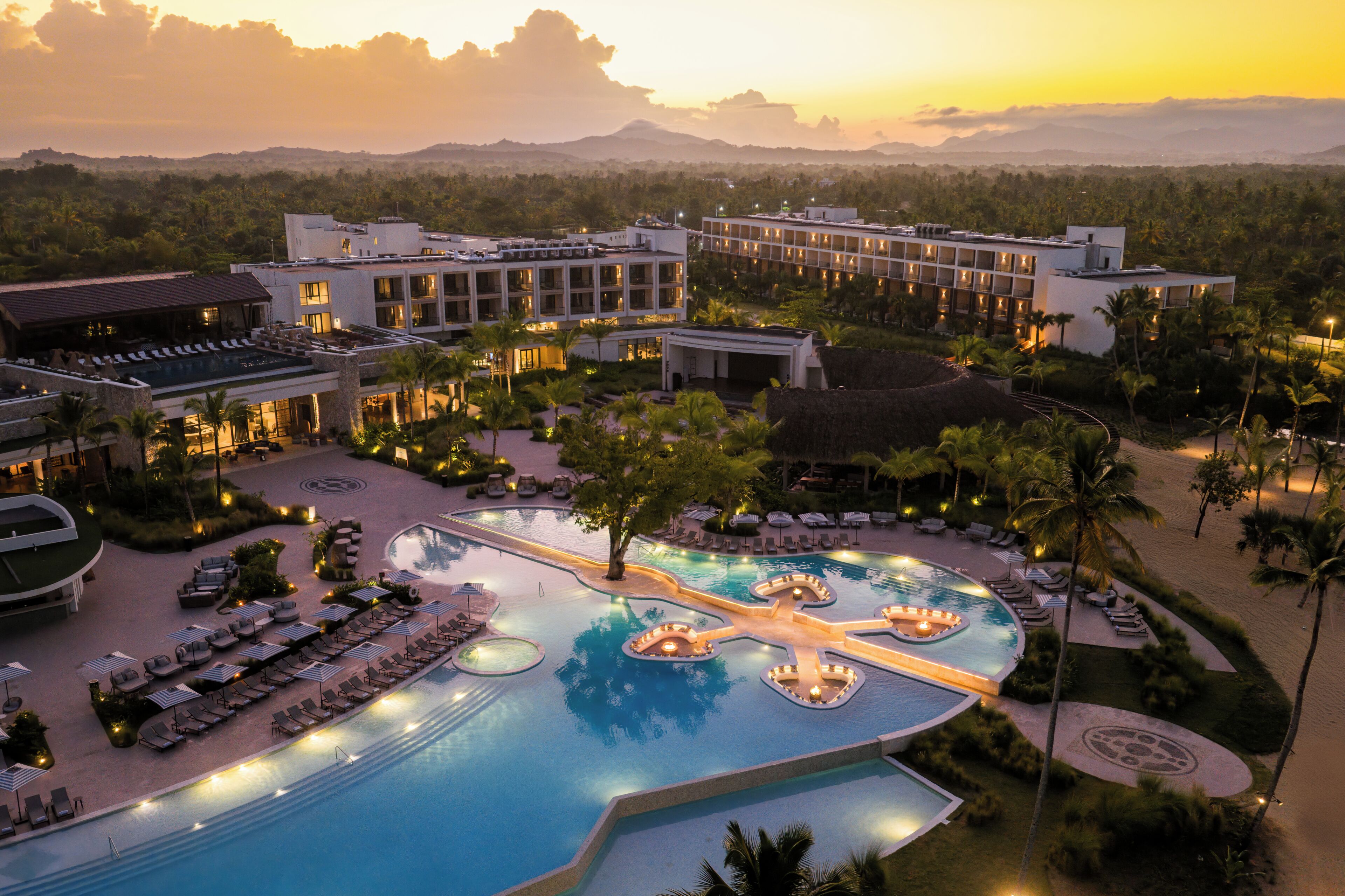 A resort with a large swimming pool, multiple lounge areas, and a view of the surrounding landscape.