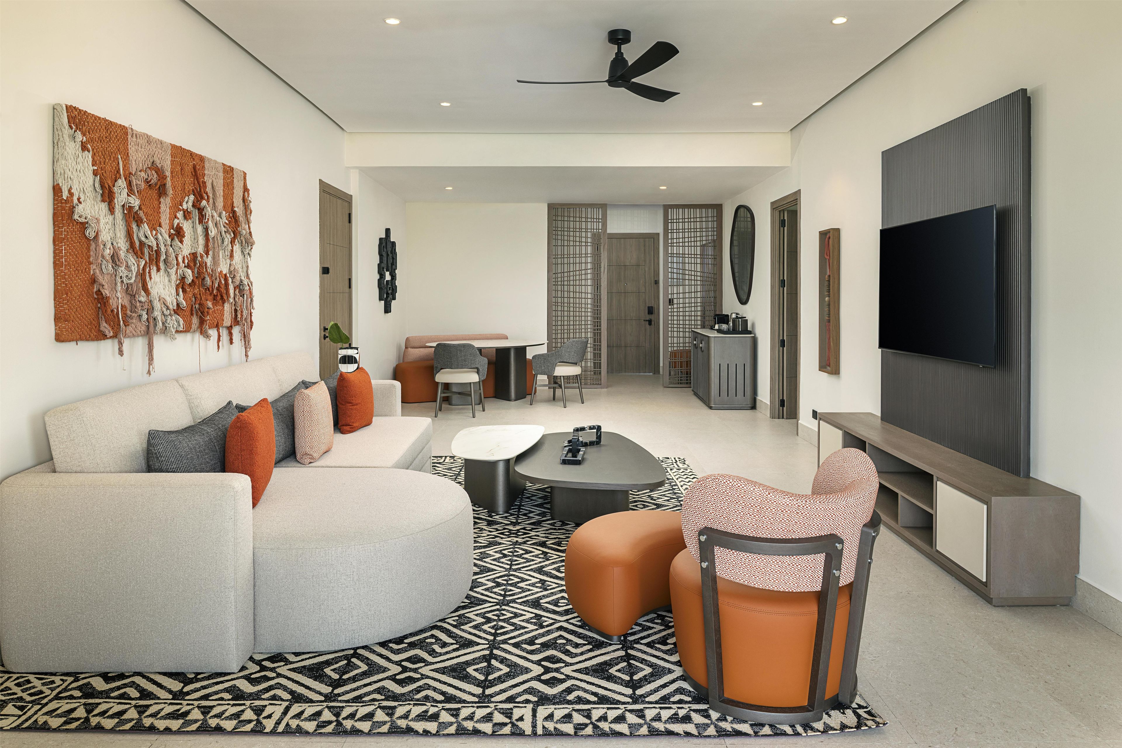Una sala de estar moderna con sofá, mesa de centro y sillas. Hay un comedor con mesa y sillas, y un televisor montado en la pared.