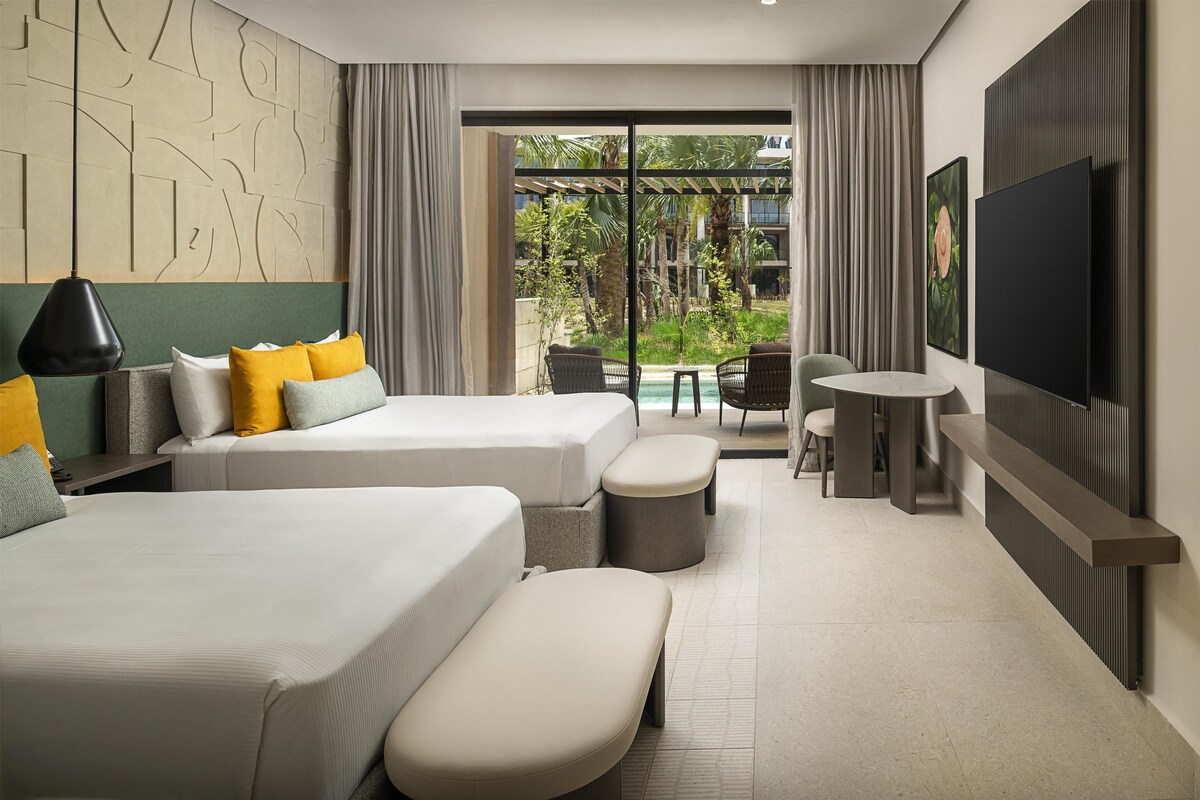 Quarto de hotel moderno com duas camas, televisão, uma mesa pequena e vista para uma piscina e área verde.