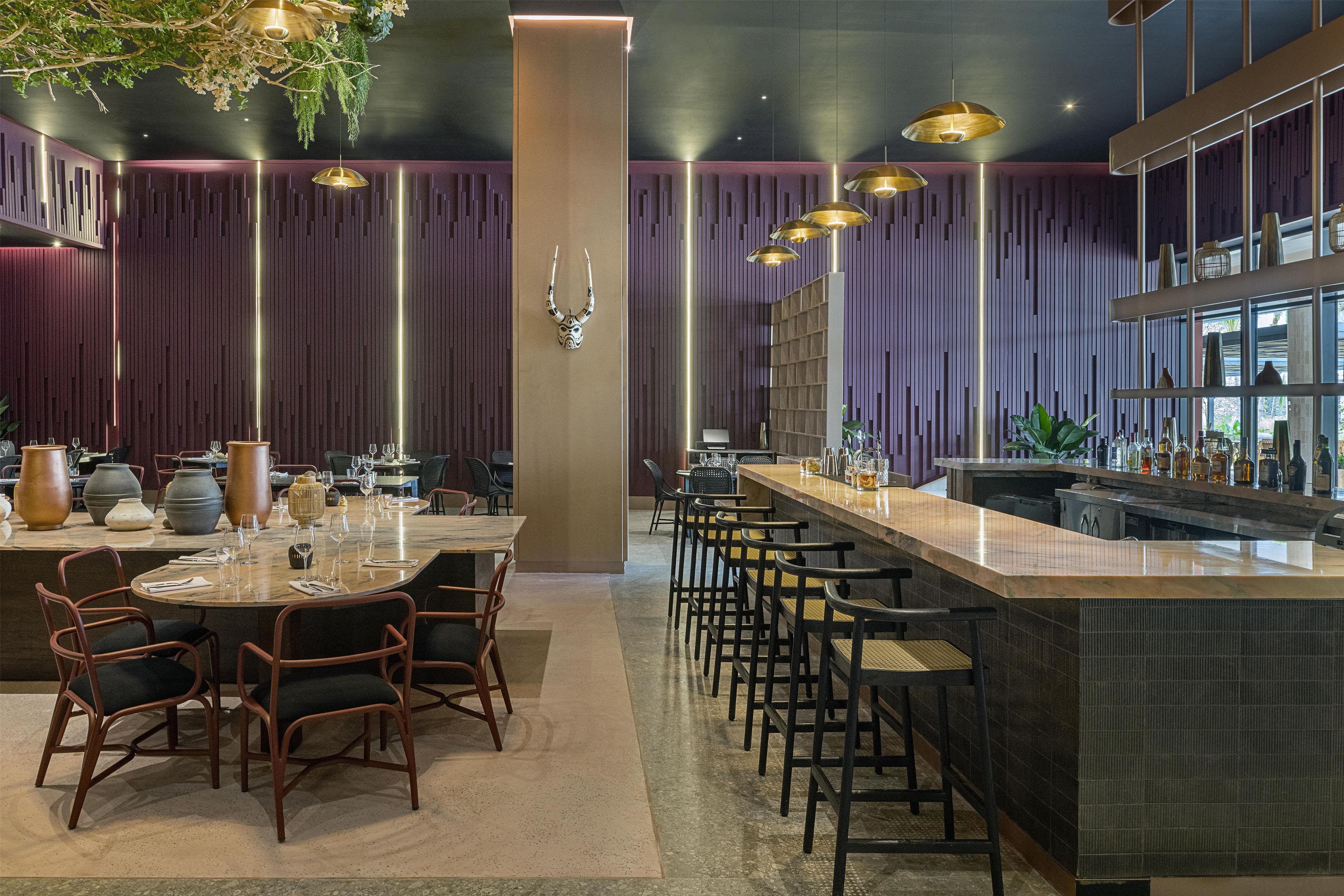 Een modern restaurantinterieur met een bar, eettafels en stoelen.
