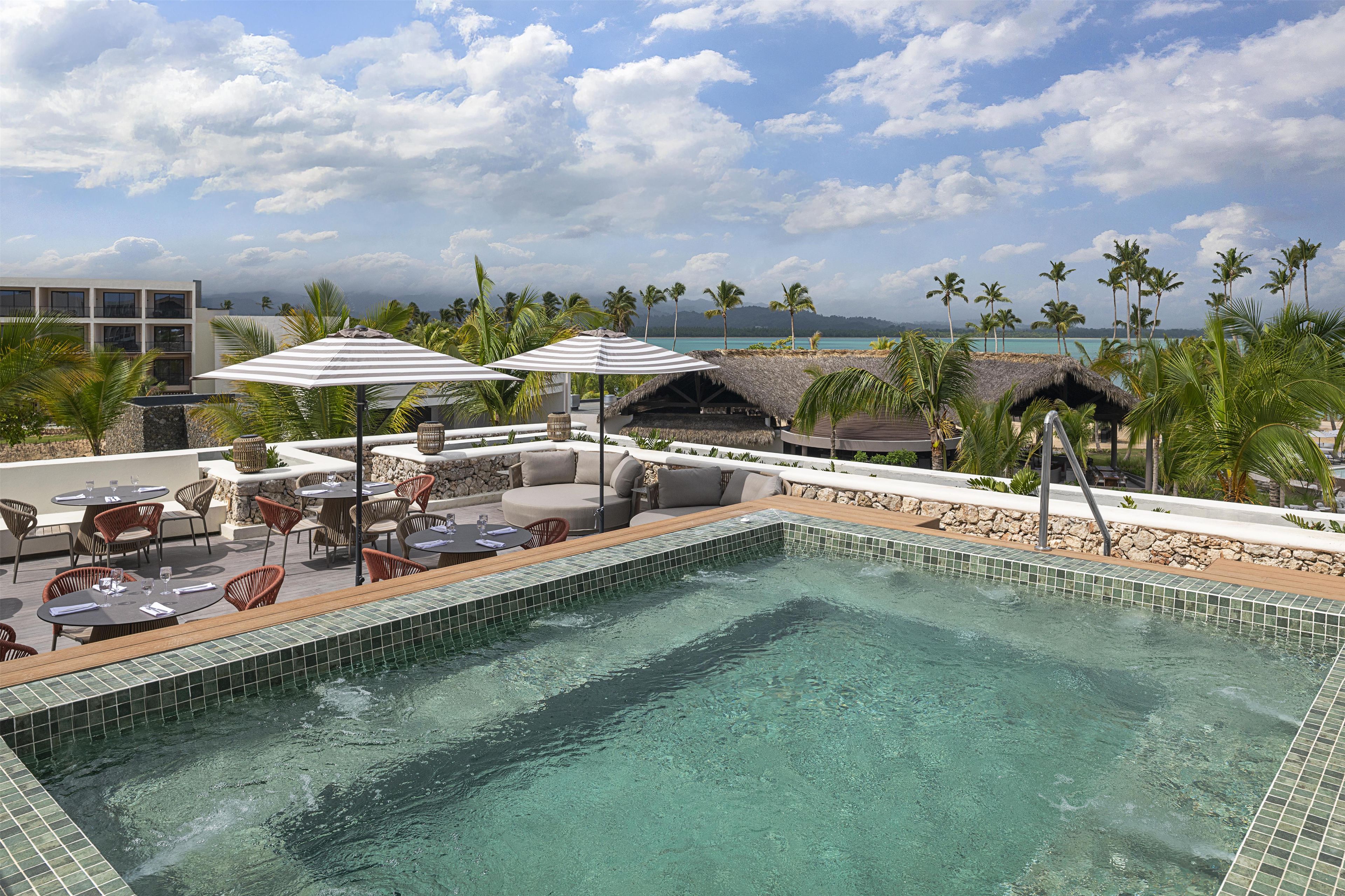 Área de piscina no terraço com espreguiçadeiras, guarda-sóis e vista para o oceano.