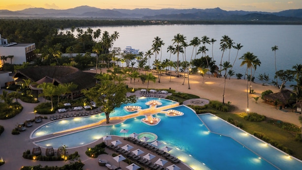 A resort with a large infinity pool, palm trees, and a view of the water.