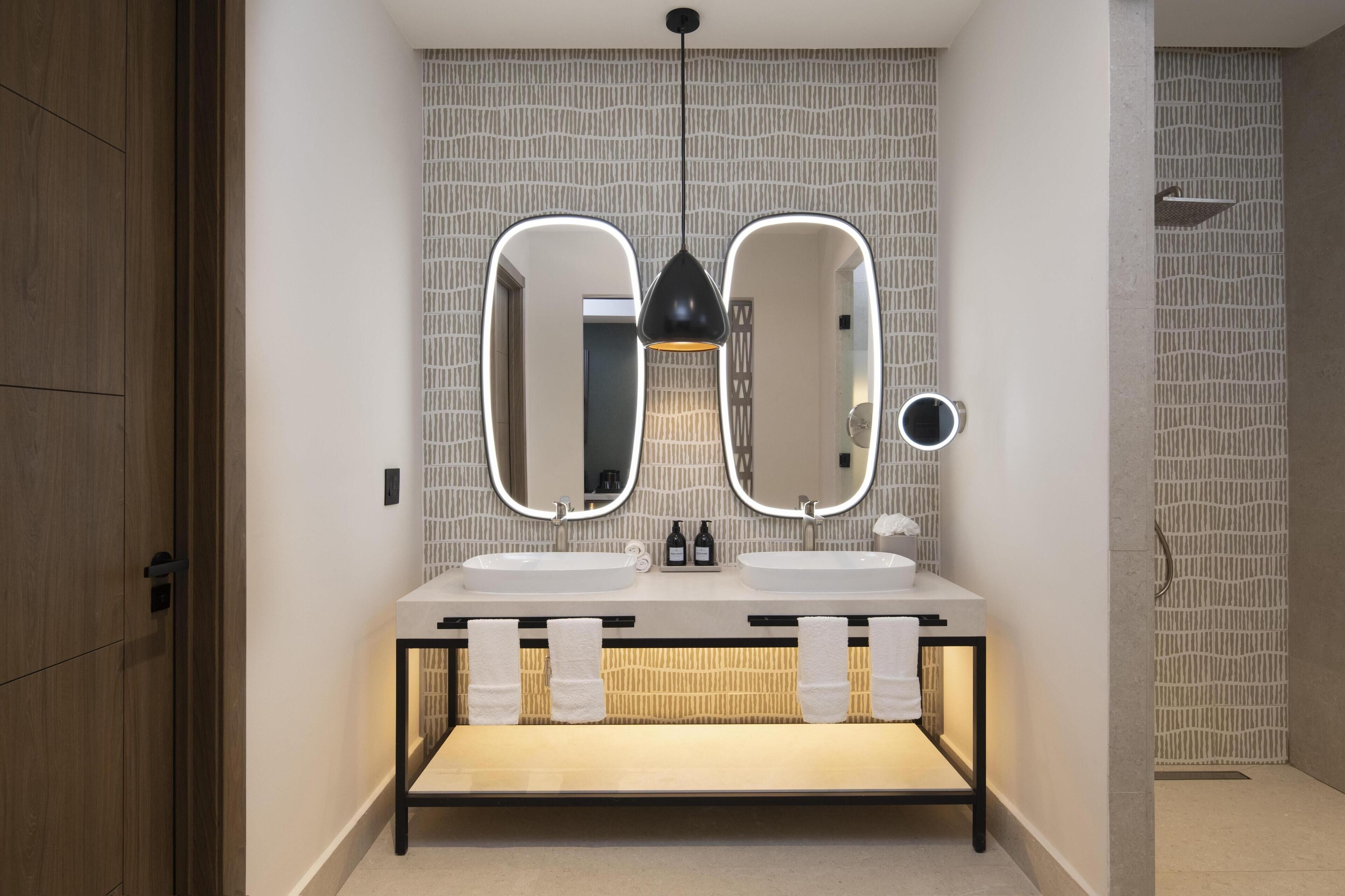 Un baño moderno con dos lavamanos, tocador y espejo con iluminación integrada.