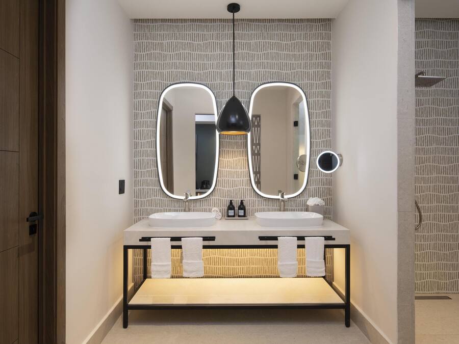 Un baño moderno con dos lavamanos, tocador y espejo con iluminación integrada.