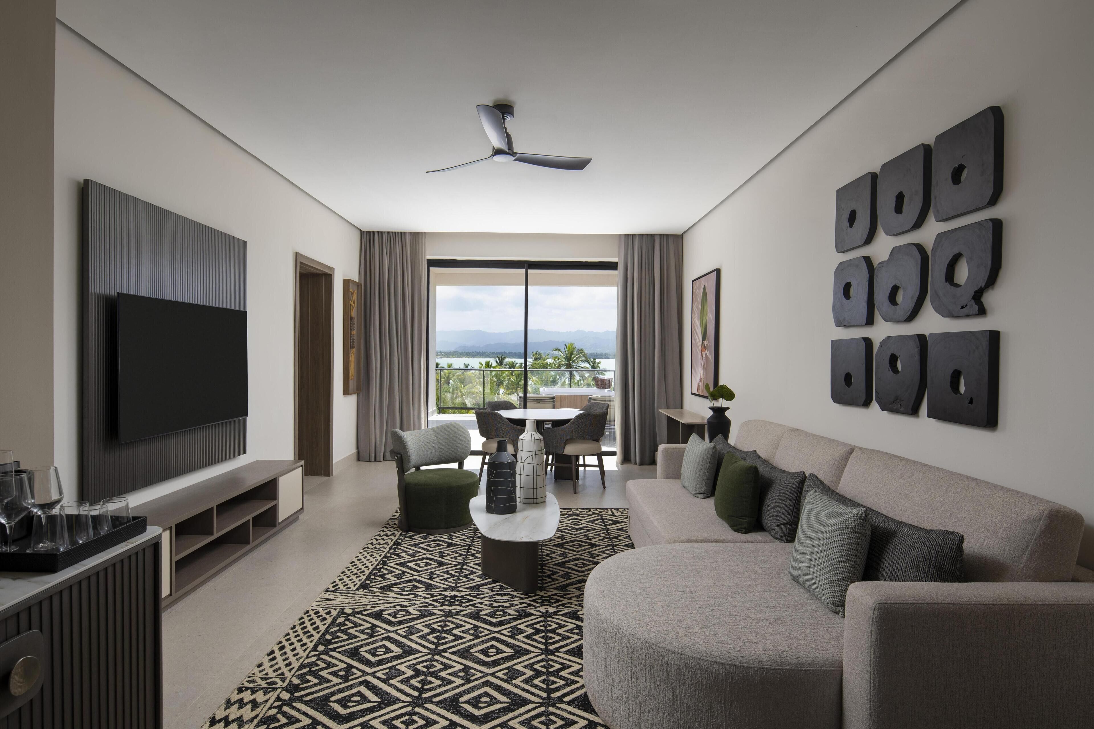 A modern living room with a flat-screen TV, a ceiling fan, a patterned rug, and a sofa with multiple cushions.