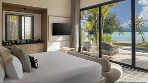 A modern hotel room with a large bed, a TV, a balcony with a view of the sea, and a seating area.