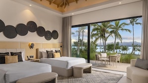 A modern hotel room with two beds, a large window with a view of palm trees and mountains, and a balcony with seating.