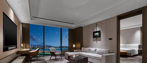 A modern living room with a large flat-screen TV, a sofa, a coffee table, and a view of a cityscape at dusk.
