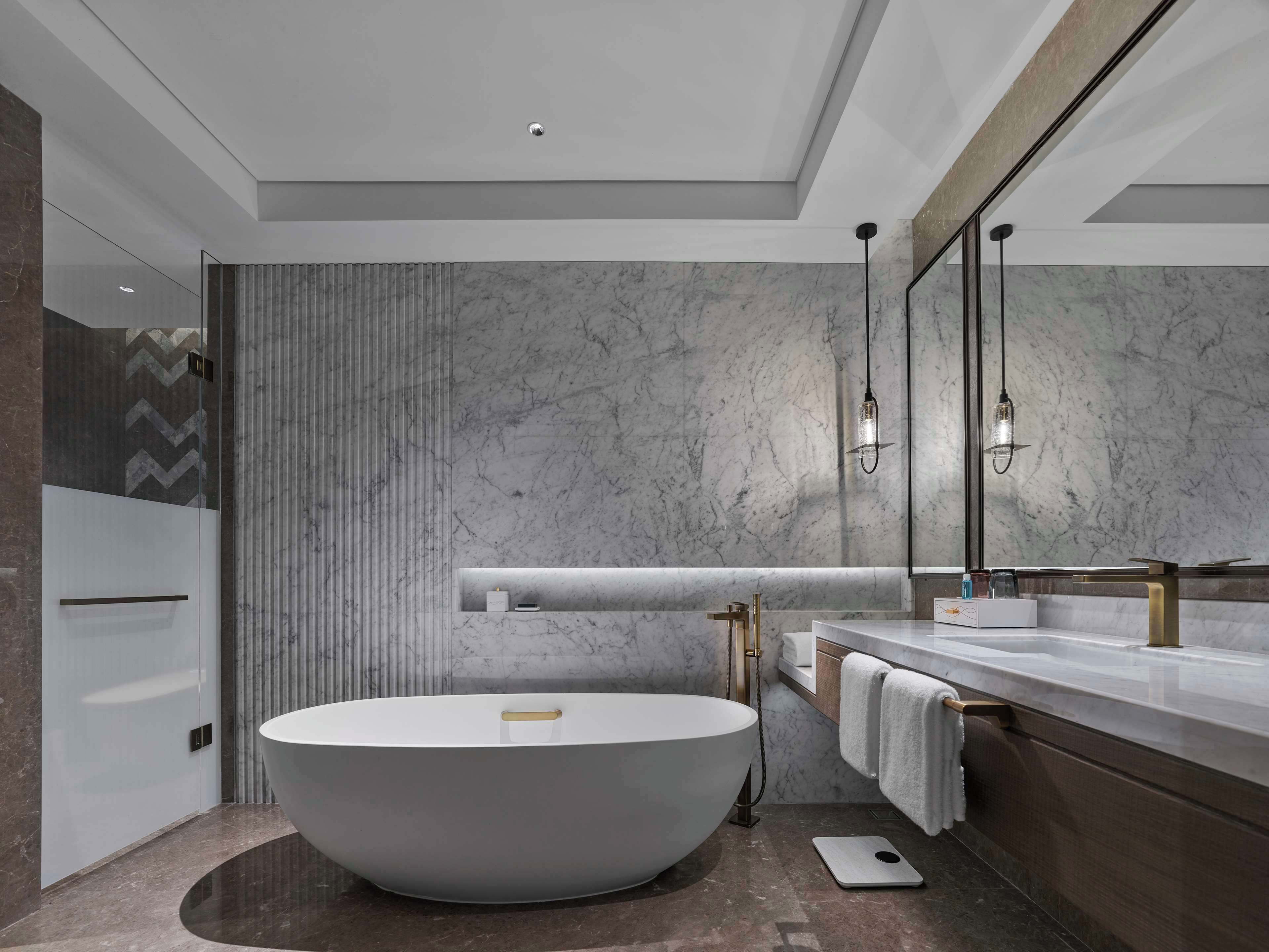 Un baño moderno con una bañera independiente, un espejo grande y un lavamanos con grifo dorado.