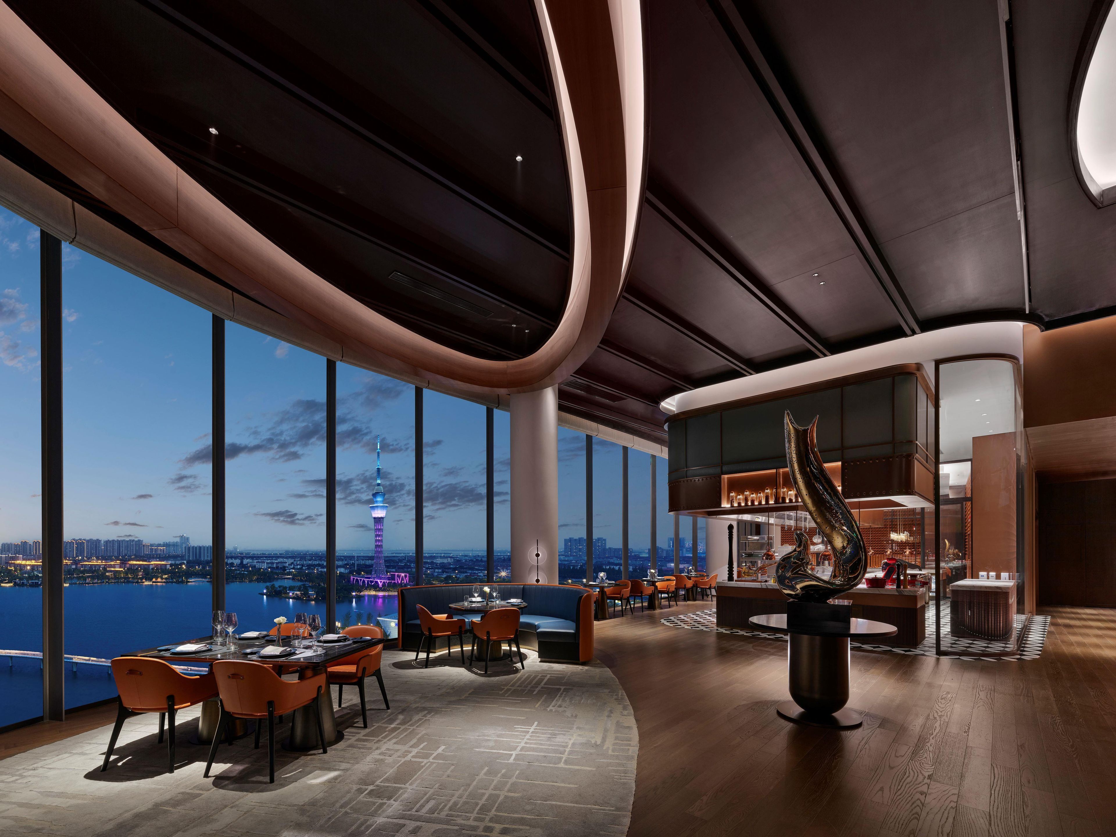 A modern interior with a panoramic view of a city skyline and a tower, featuring a bar area and seating arrangements.
