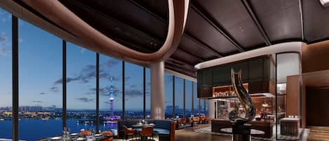 Un interior moderno con vistas panorámicas de un horizonte urbano y una torre, con zona de bar y disposición de asientos.