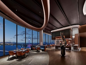 A modern interior with a panoramic view of a city skyline and a tower, featuring a bar area and seating arrangements. - Hilton Changshu (Suzhou)