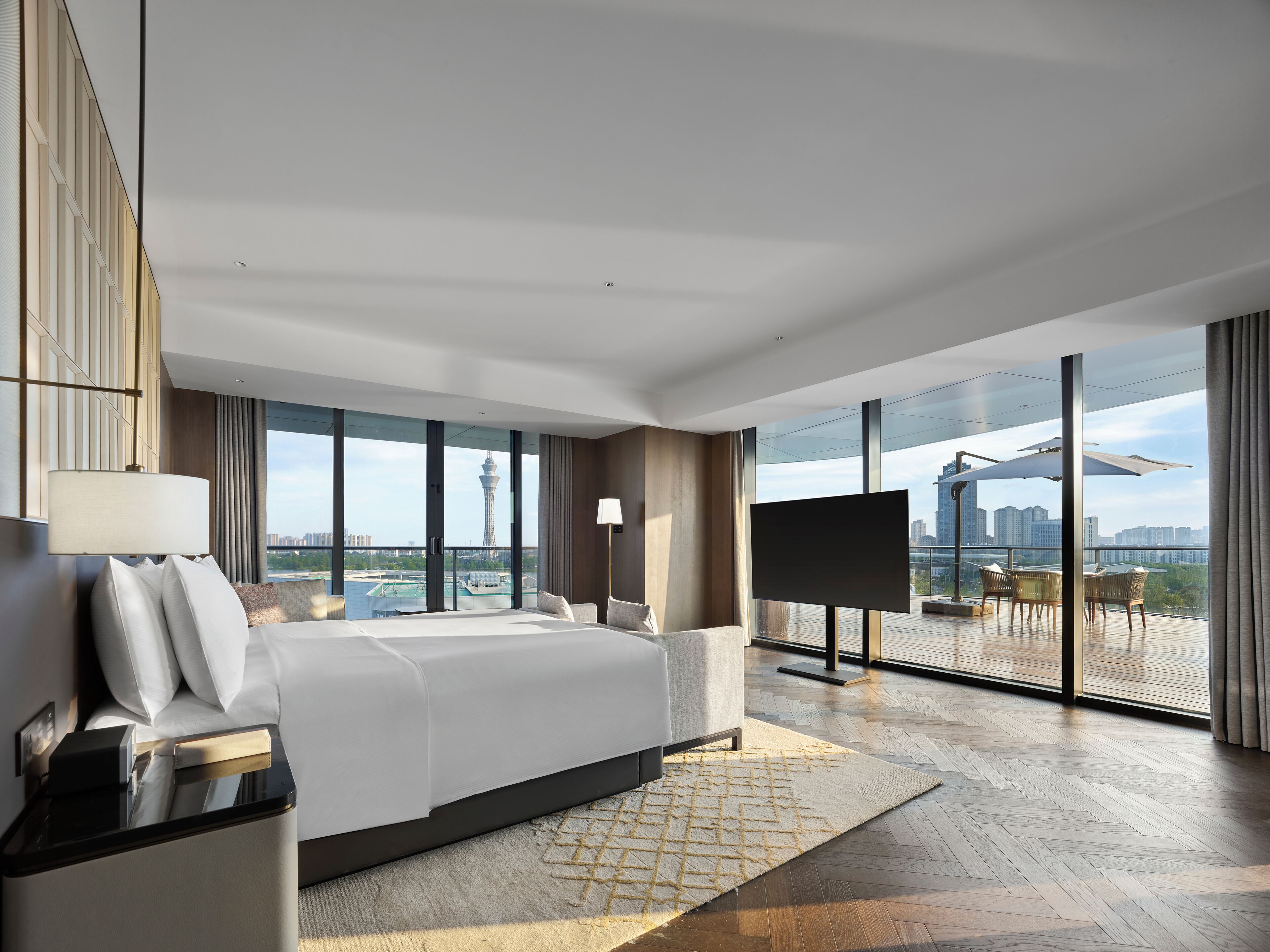 A modern hotel room with a large bed, a TV, and a balcony with a city view.