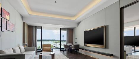 A modern living room with a large flat-screen TV, comfortable seating, and a view of a cityscape through large windows.