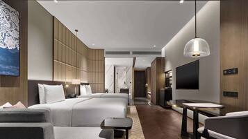 A modern hotel room with a large bed, a TV, a desk, and a seating area.